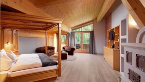 A wooden four-poster bed in a room with a large window, a fireplace, and a kitchen area. - Adler Inn Tyrol Mountain Resort SUPERIOR (Tux)