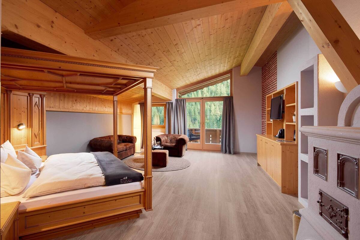 Una cama con dosel de madera en una habitación con un ventanal grande, chimenea y zona de cocina.