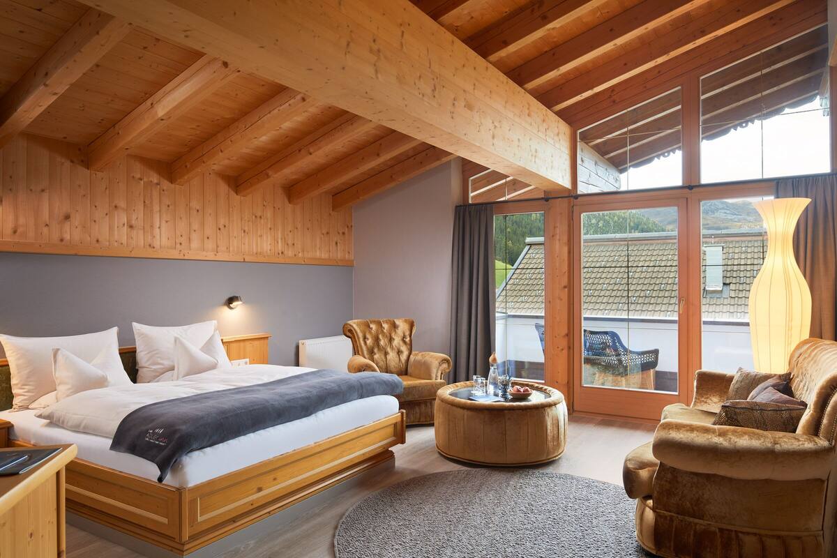 Un dormitorio moderno con techo de madera, una cama grande, una mesita redonda y un sofá.