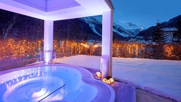 A hot tub under a covered area with a snowy mountain backdrop and string lights. - Adler Inn Tyrol Mountain Resort SUPERIOR (Tux)