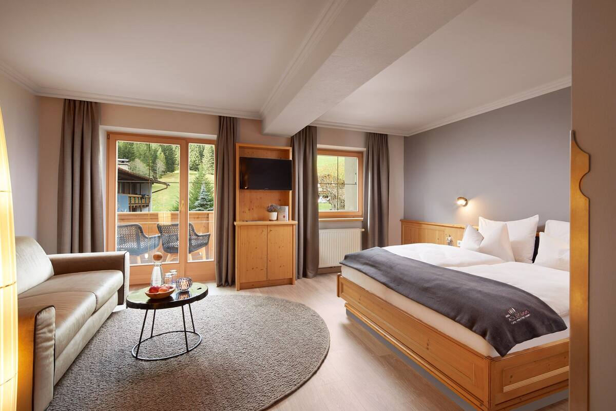 Habitación de hotel con cama, sofá, una mesita con un frutero, televisor y vistas al exterior.