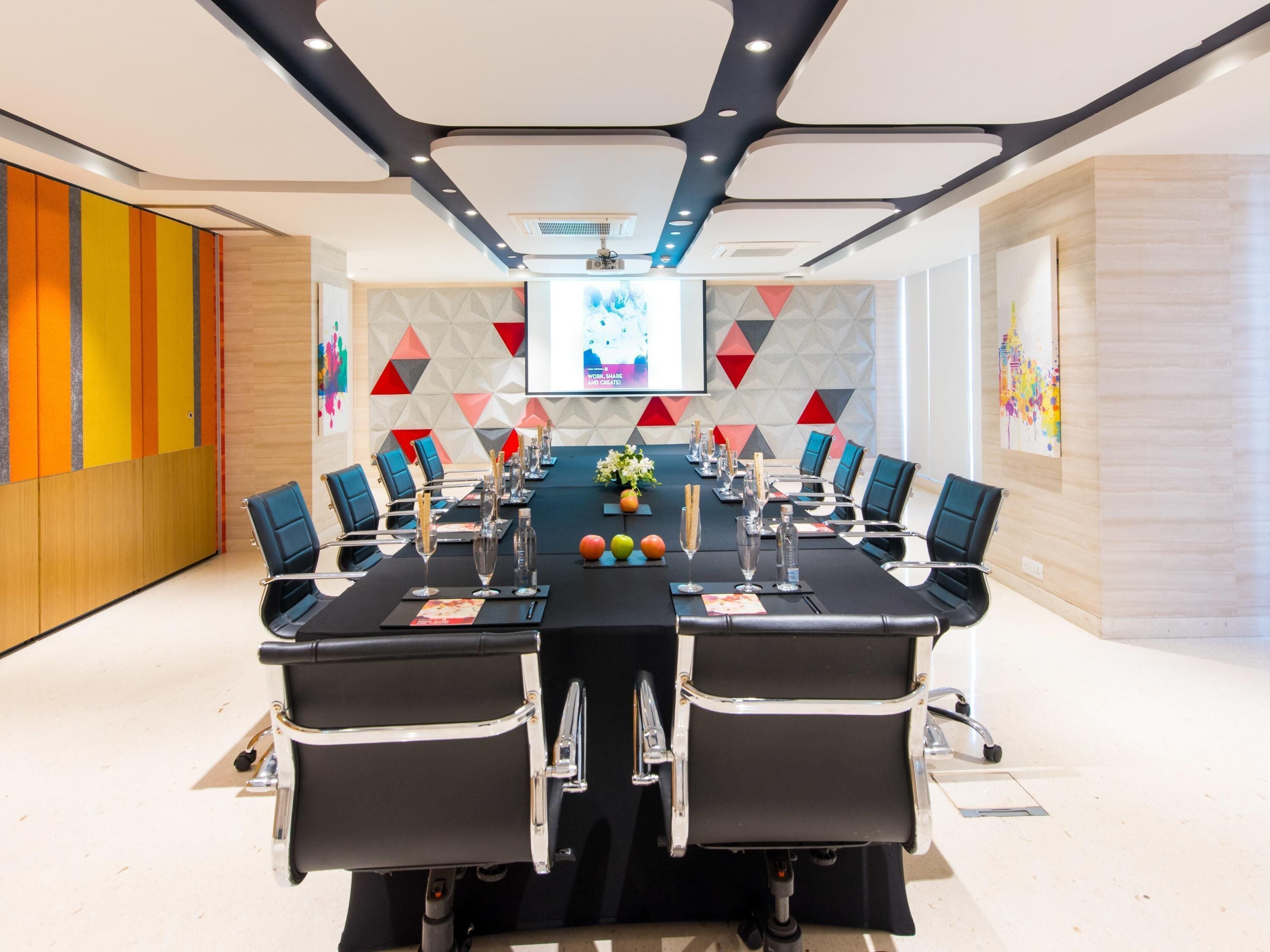 A conference room with a long table, chairs, and a projector screen.