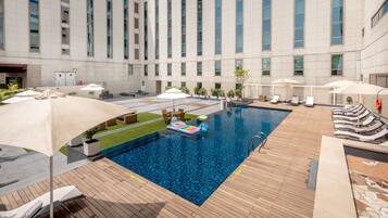 Relax by the pool surrounded by lounge chairs and umbrellas, with a view of the adjacent building.