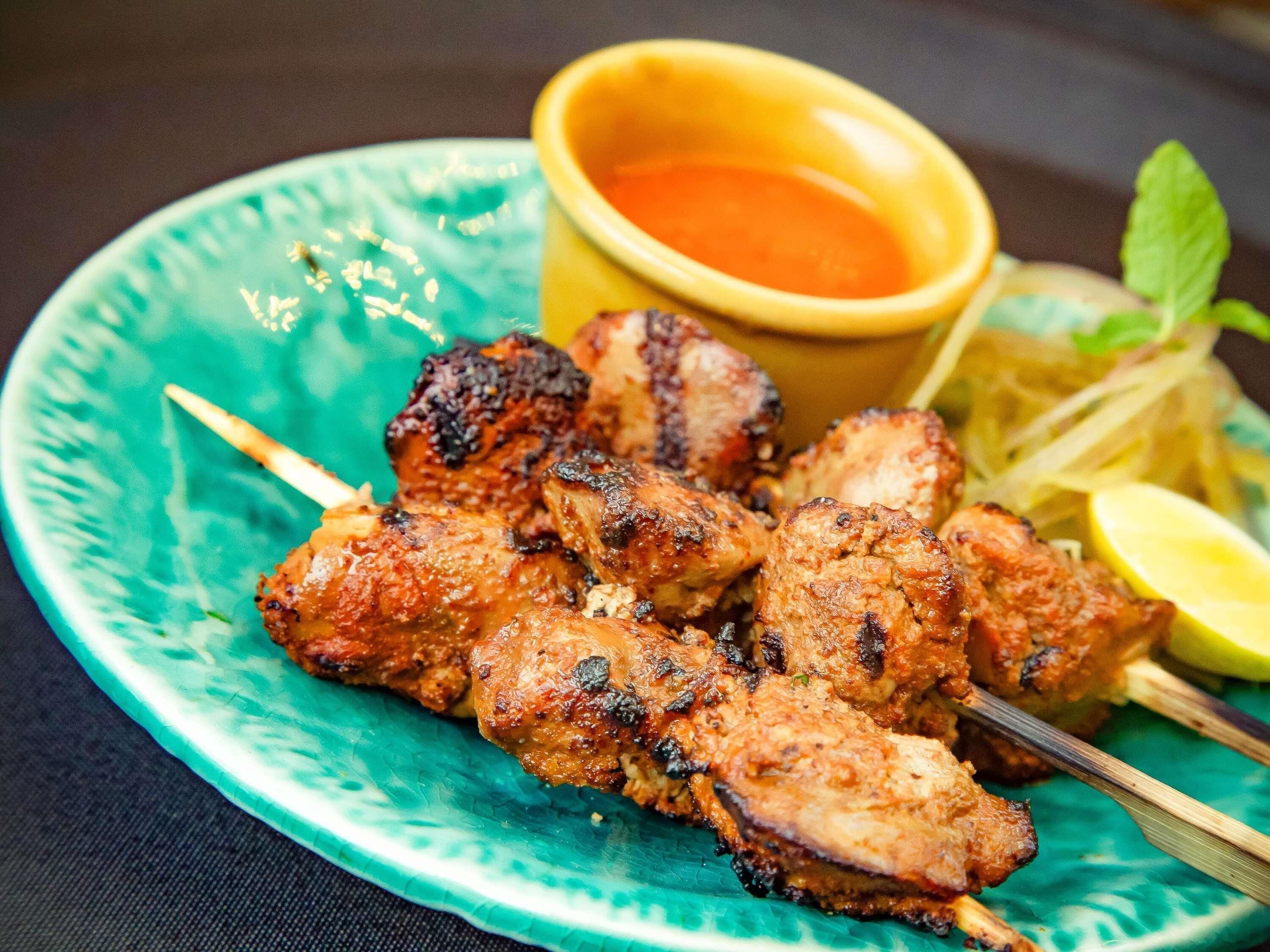 Grilled meat skewers on a plate with a dipping sauce and lemon wedges.