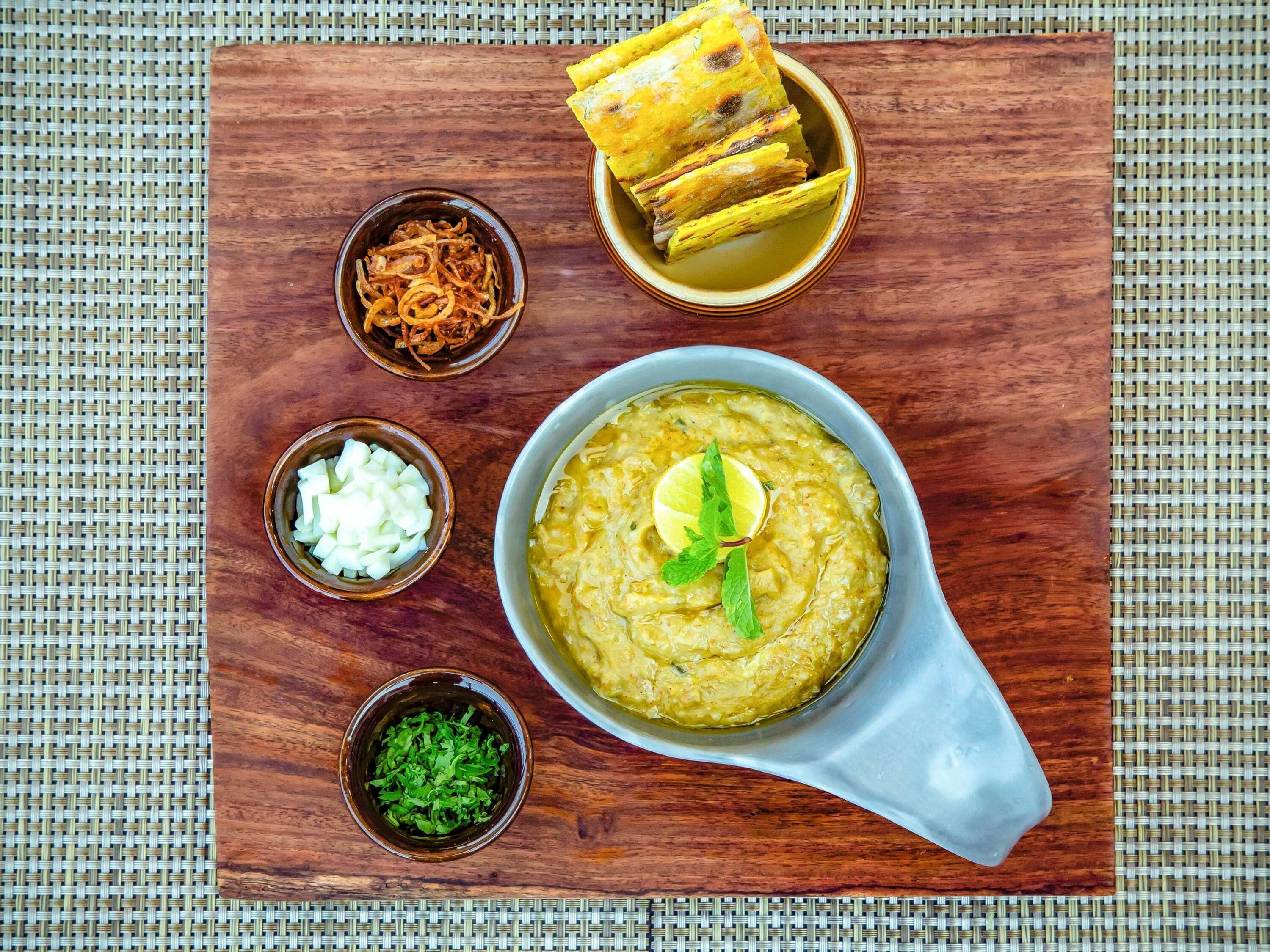 Un repas composé d’une soupe agrémentée d’une tranche de citron vert et de menthe, accompagné de pain frit, d’oignons frits et d’un petit bol d’oignons hachés.