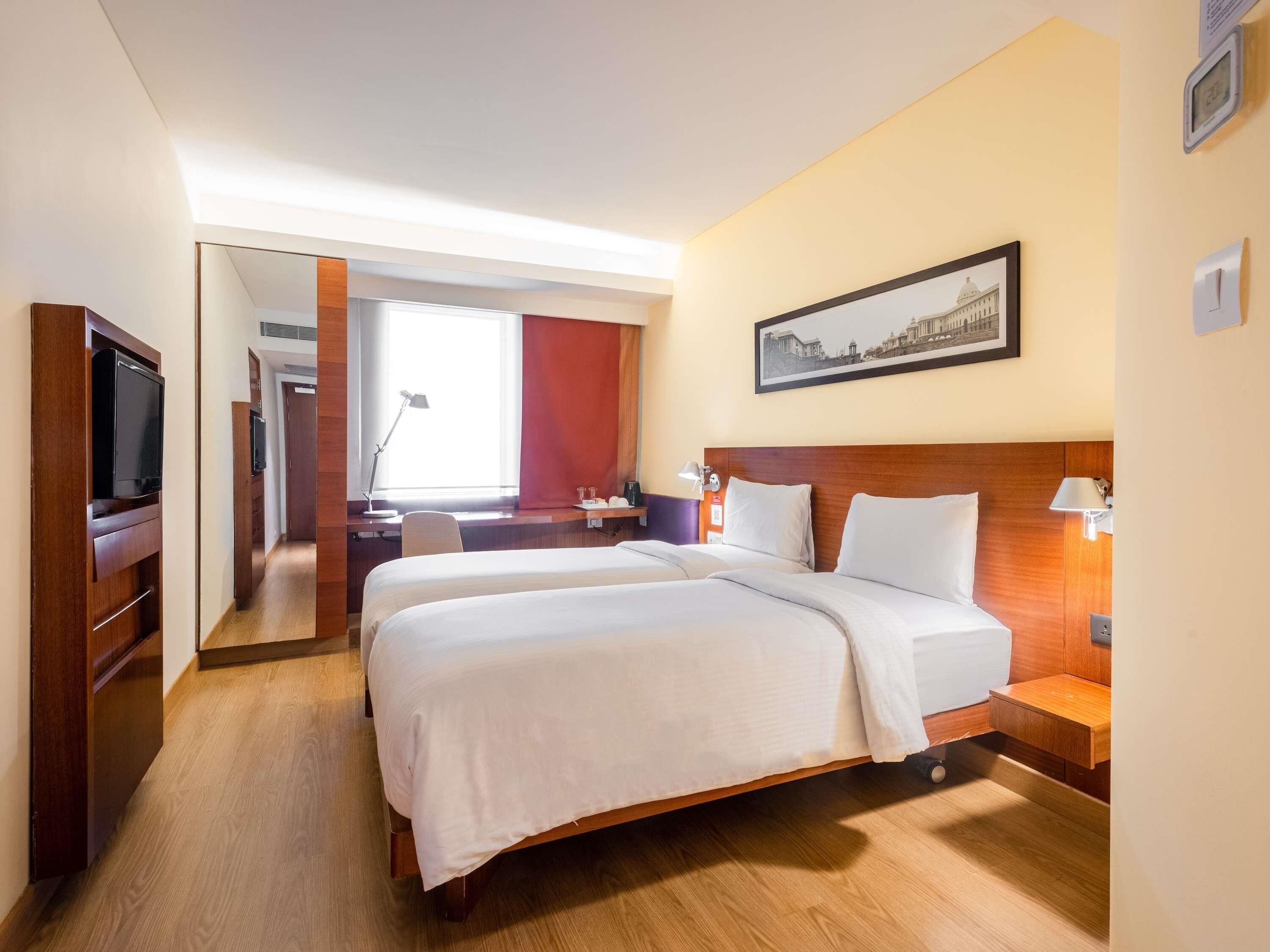 A hotel room with two beds, a desk, a TV, and a framed picture on the wall.