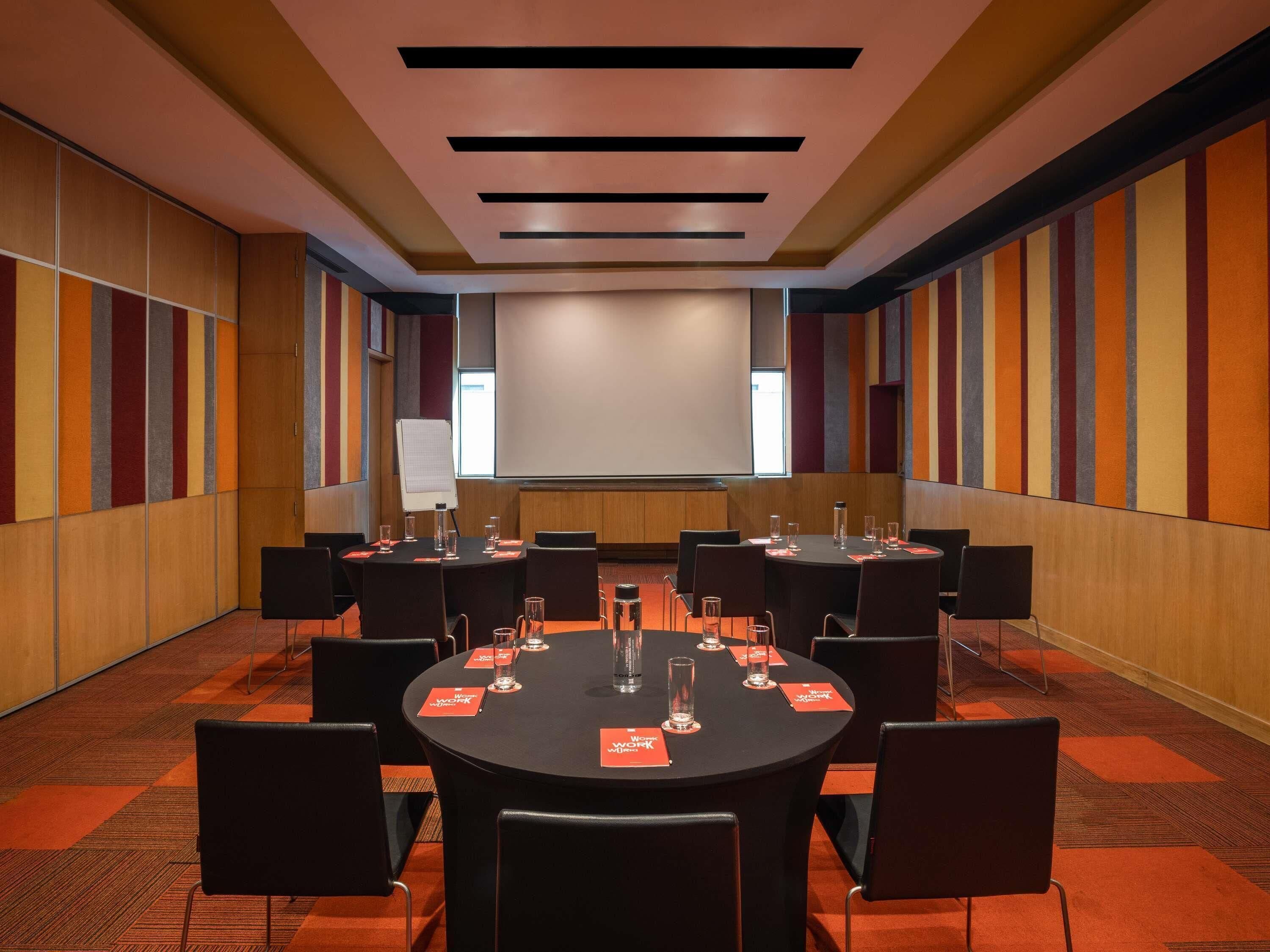 A conference room with a large screen, round tables, and chairs.