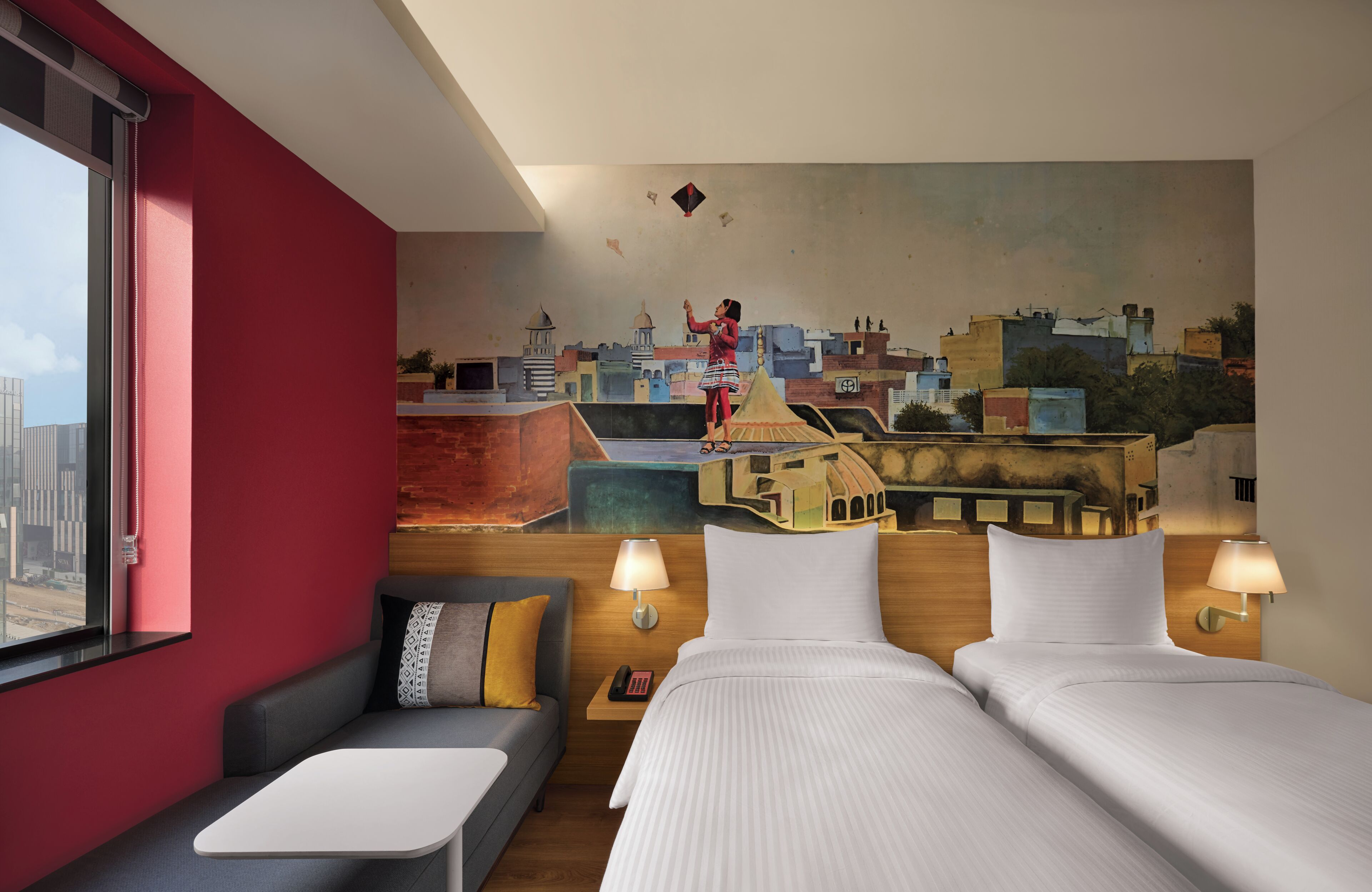 A hotel room with a cityscape mural, a sofa, two beds, and bedside lamps.