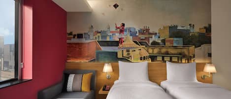 A hotel room with a cityscape mural, a sofa, two beds, and bedside lamps.