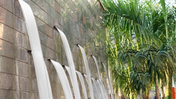 Un élément décoratif aquatique composé de plusieurs cascades d’eau dévalant un mur, le tout entouré de palmiers.