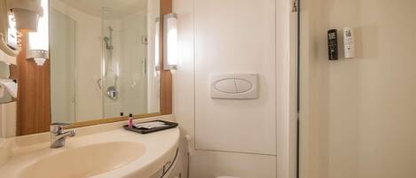 A bathroom with a sink, mirror, toilet, shower, and a wall-mounted control panel.