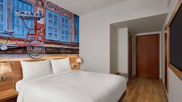 A hotel room with a bed, a wall-mounted lamp, a wooden headboard, and a mural of a bicycle.