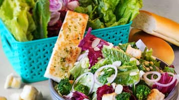 A bowl of salad with various vegetables and croutons, a piece of grilled bread, and a baguette on a table.