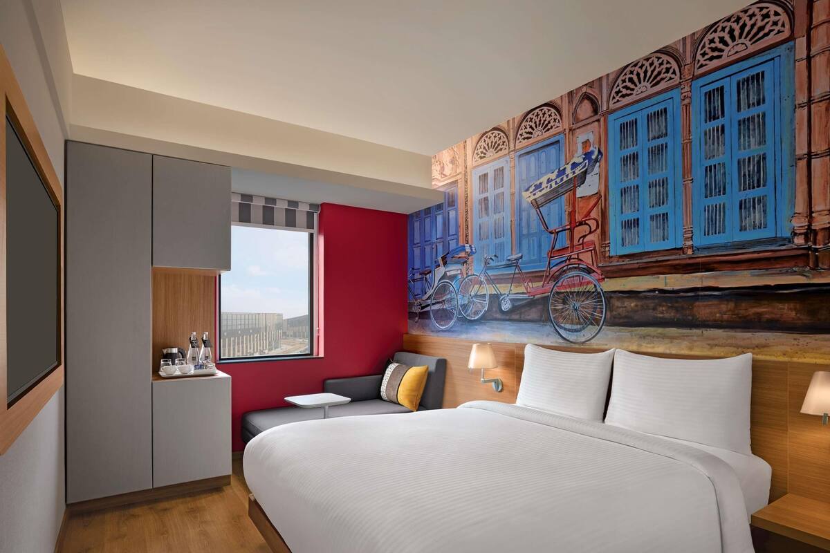 Ein Hotelzimmer mit einem großen Bett, einer Sitzecke, einem Esstisch und einem Wandbild mit Fahrrädern.