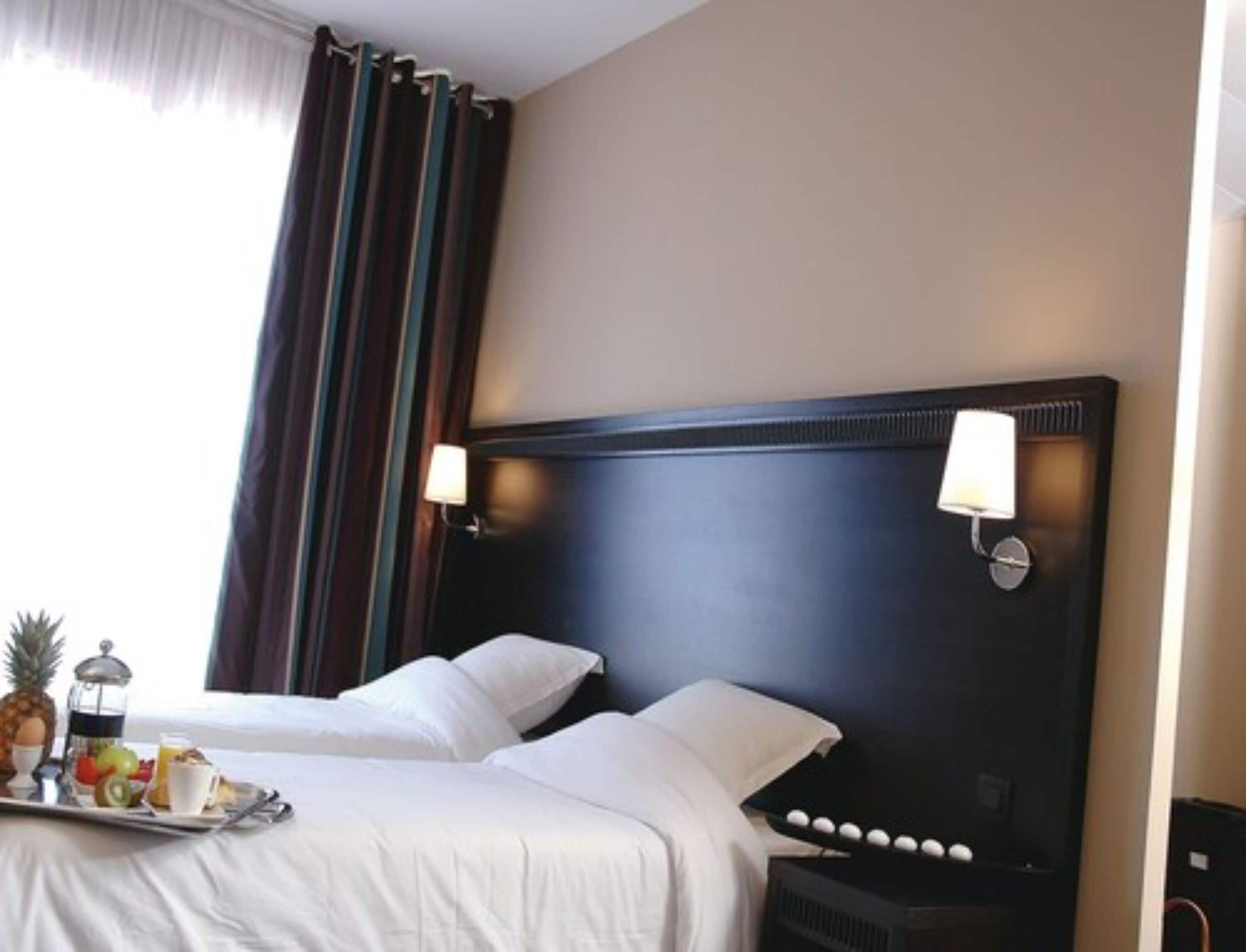 A hotel room with a large bed, two bedside lamps, a tray with breakfast items, and a window with curtains.
