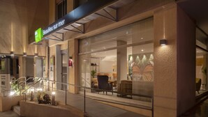 A hotel entrance with a glass facade, outdoor seating area, and a staircase leading to the entrance. - ibis Styles Beaulieu Sur Mer (Beaulieu-sur-Mer)