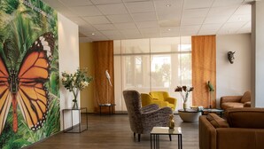 A modern lobby with a large butterfly mural, comfortable seating, and a large window providing natural light. - ibis Styles Beaulieu Sur Mer (Beaulieu-sur-Mer)