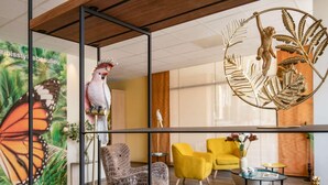 A modern interior with a glass partition, a decorative metal sculpture, a vibrant butterfly mural, and a yellow armchair. - ibis Styles Beaulieu Sur Mer (Beaulieu-sur-Mer)