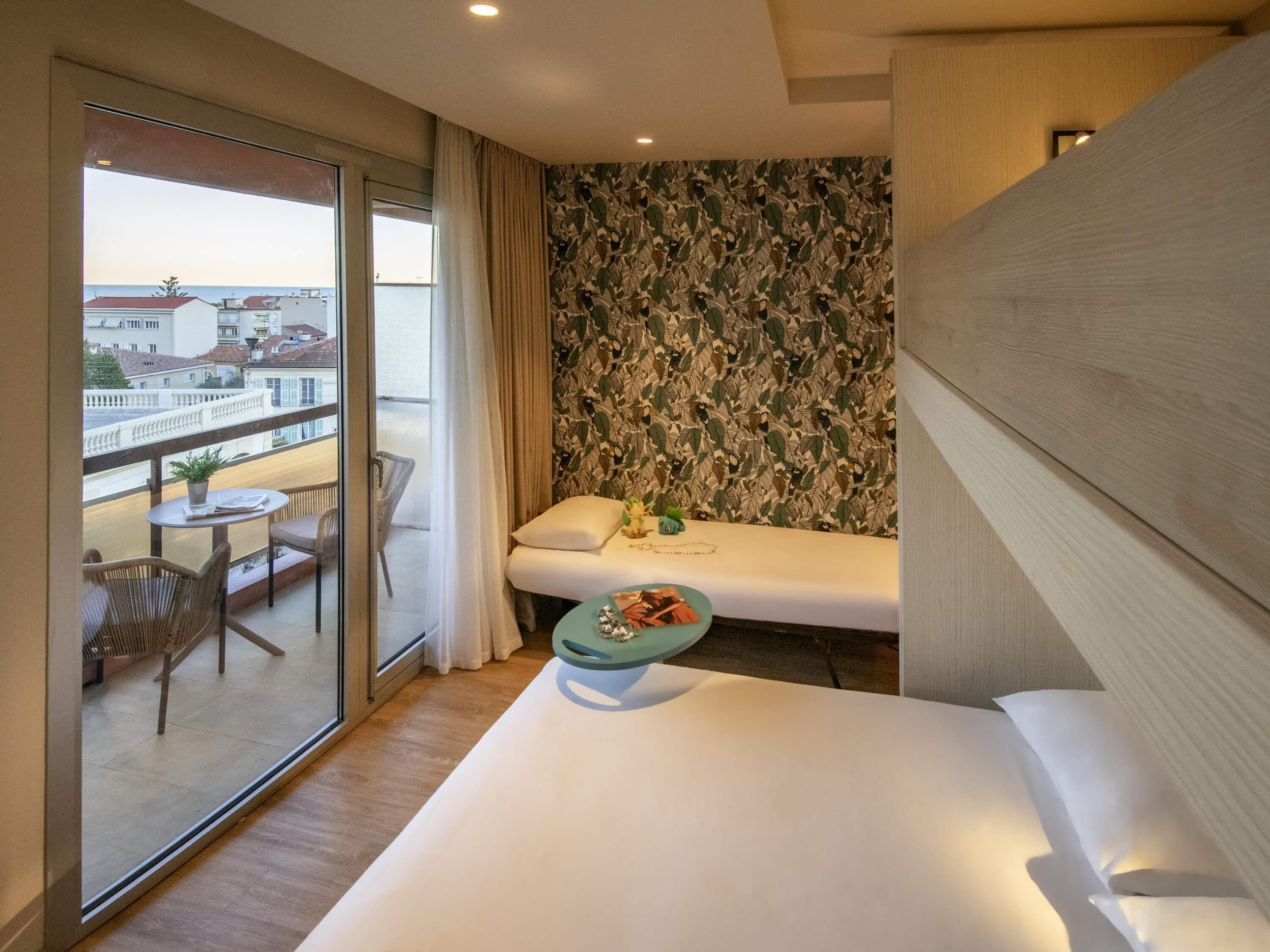 A hotel room with a balcony, a bed, a small table with a plant, and a patterned wall.
