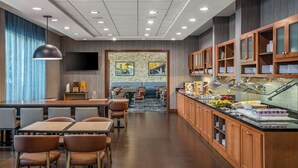 A modern hotel dining area with a buffet, seating, and a TV.