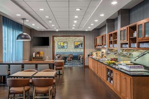 Un espace repas moderne dans un hôtel, avec un buffet, des tables et un téléviseur.