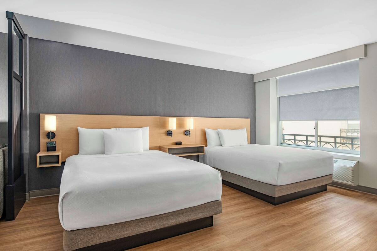 A hotel room with two beds, a large window with a view, and a modern design.