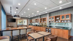 A modern restaurant with a long counter, wooden cabinets, and a tiled backsplash. - Hyatt Place Riverside Downtown (Riverside)