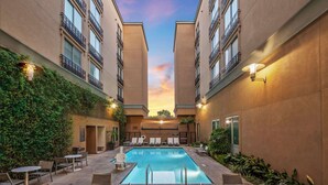 A pool area with lounge chairs and tables, surrounded by buildings with balconies and outdoor lighting. - Hyatt Place Riverside Downtown (Riverside)