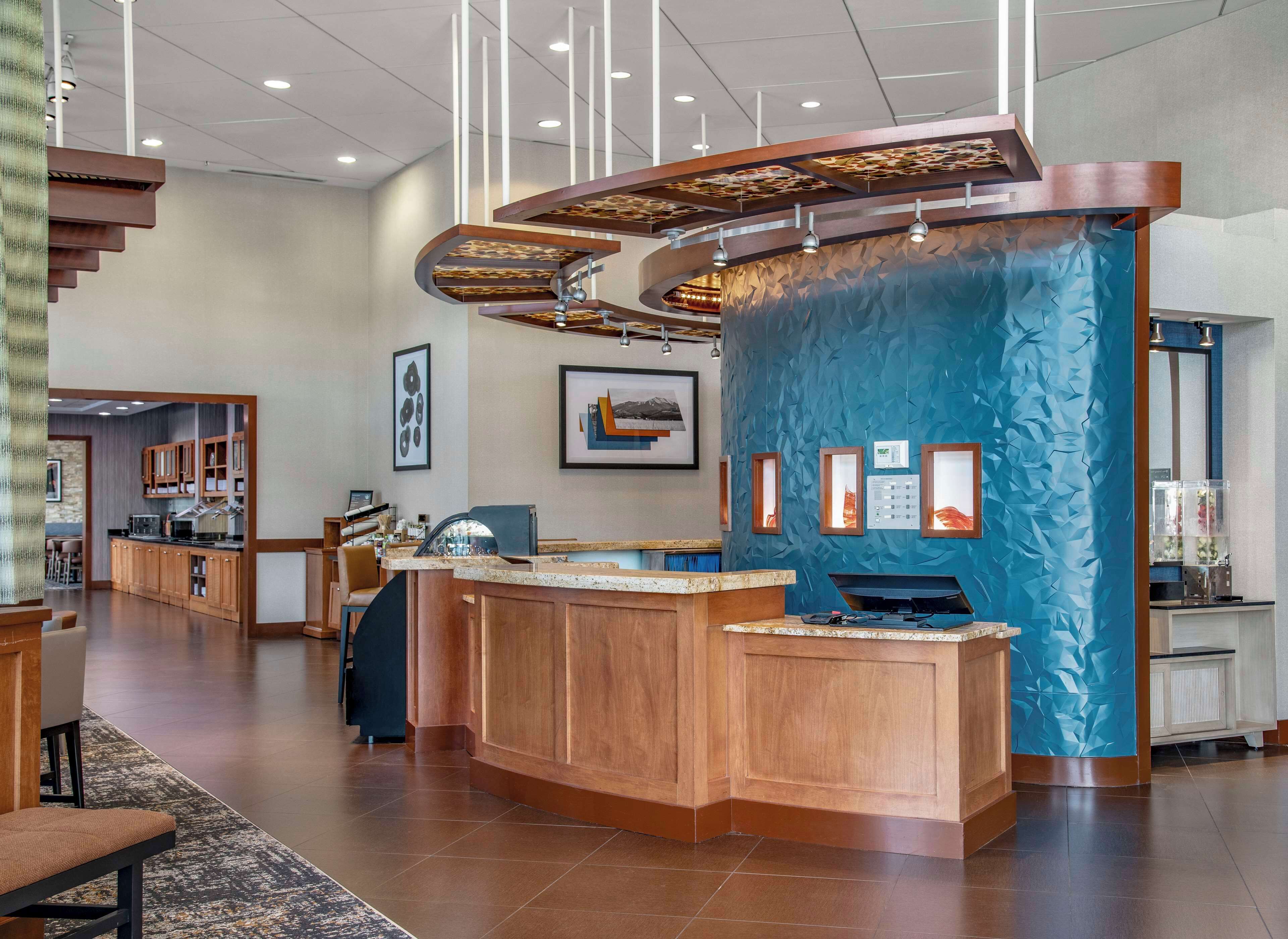 Un vestíbulo de hotel moderno con un mostrador de recepción de madera, una pared azul con textura y una escalera que conduce a pisos superiores.