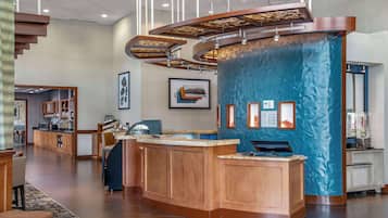 Un vestíbulo de hotel moderno con un mostrador de recepción de madera, una pared azul con textura y una escalera que conduce a pisos superiores.