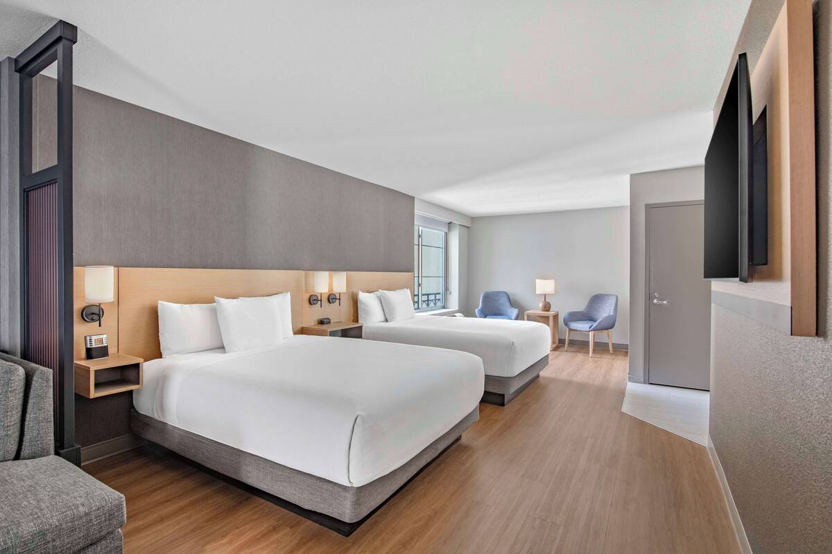 A hotel room with two beds, a desk, a chair, a TV, and a window.