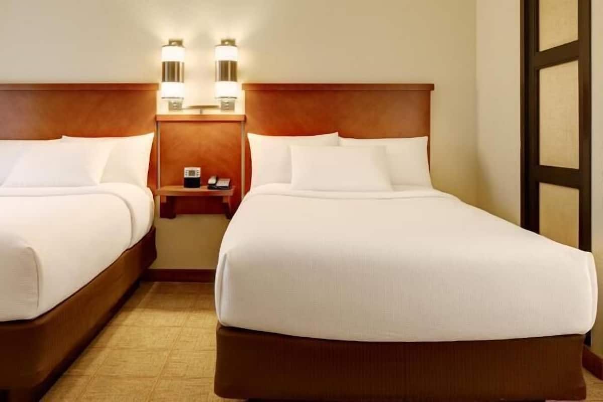 Two beds with wooden headboards, a nightstand with a phone, and wall-mounted lights.