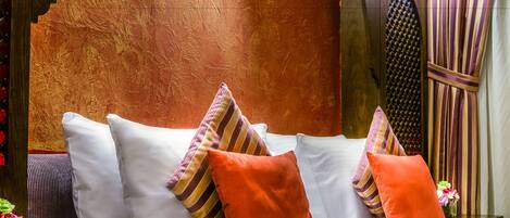 A neatly made bed with white linens and multiple pillows, including striped and solid orange ones, in a room with a textured wall and a decorative wall panel.