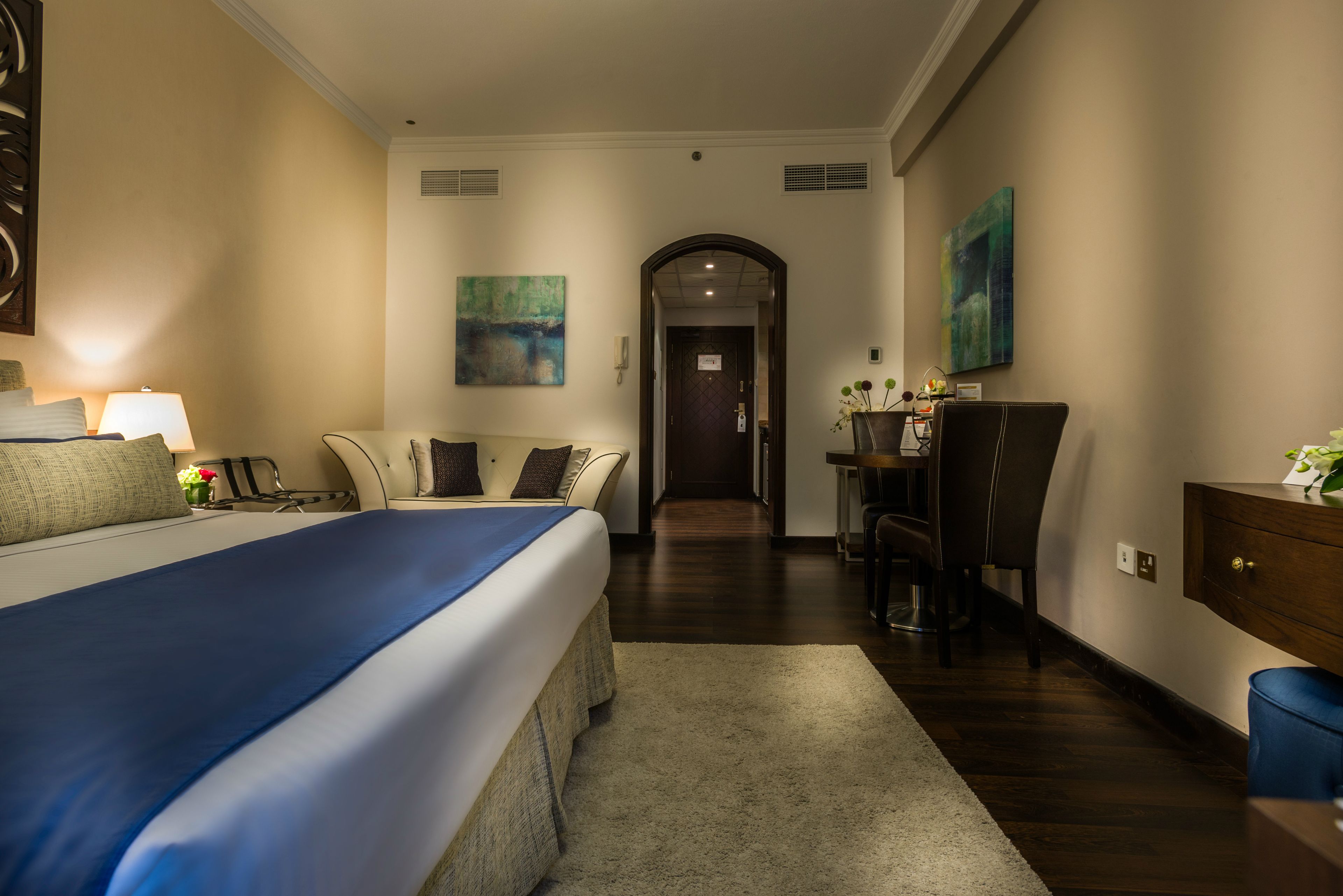 Ein Hotelzimmer mit einem großen Bett, einem Schreibtisch und einem Sessel. Eine Tür führt in einen weiteren Raum.
