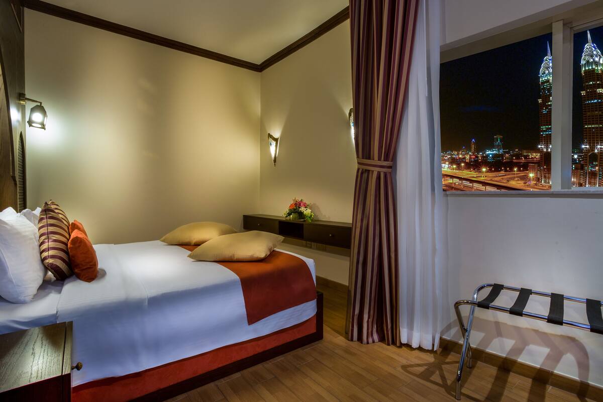 Ein Hotelzimmer mit Bett, Fenster mit Blick auf die Stadt und Nachttisch mit Lampe.