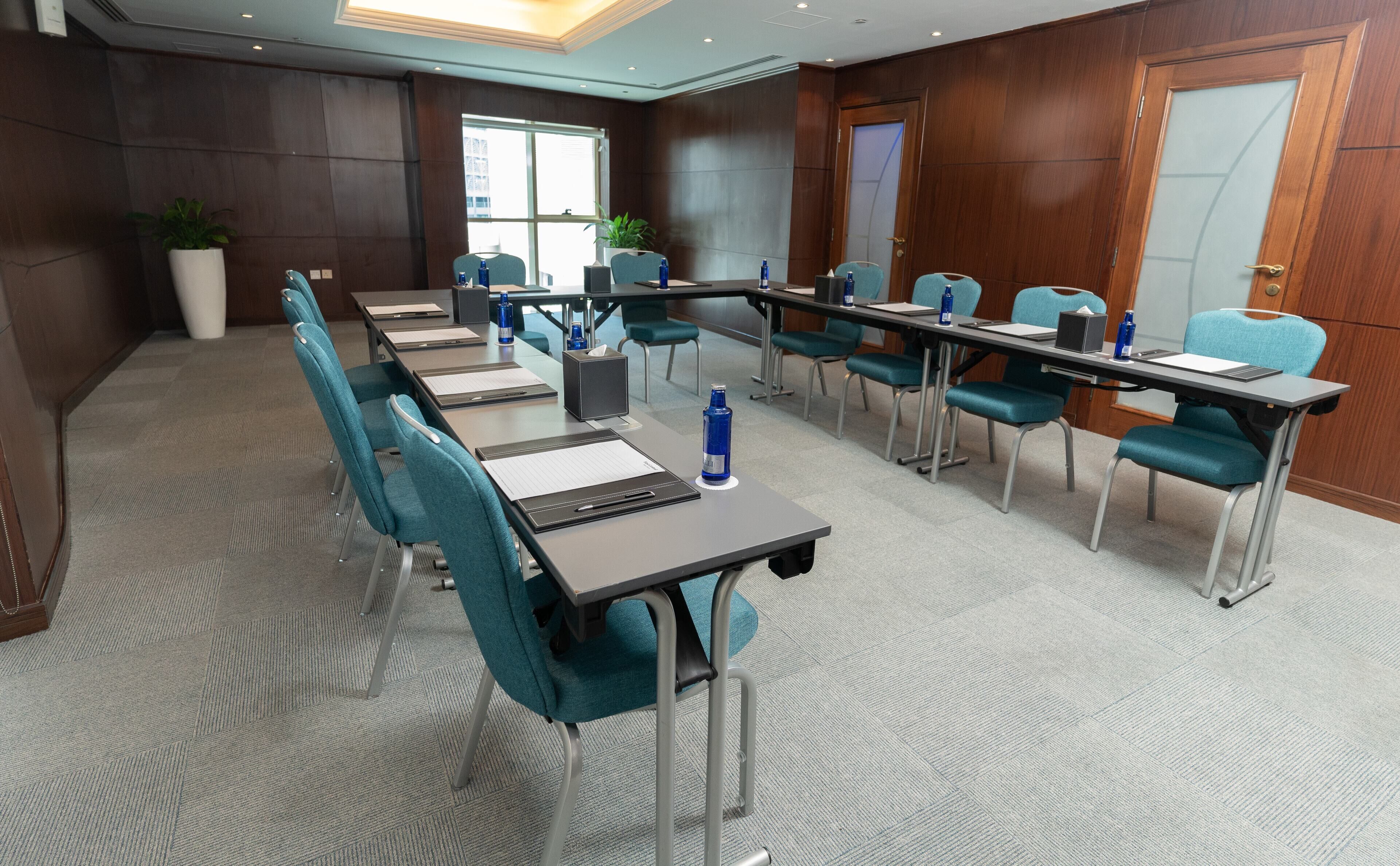 A conference room with a long table, teal chairs, and a carpeted floor.