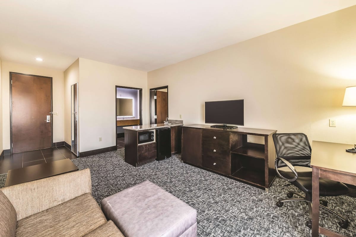 Ein Hotelzimmer mit Sofa, kleinem Tisch, Schreibtisch mit Stuhl, Fernseher und Minibar.