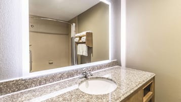 A bathroom with a granite countertop, a sink, a mirror, and a shower area.