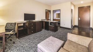 A hotel room with a flat-screen TV, a desk with drawers, a mirror, a sofa, and a door. - La Quinta Inn & Suites by Wyndham Tulsa - Catoosa Route 66 (Catoosa)