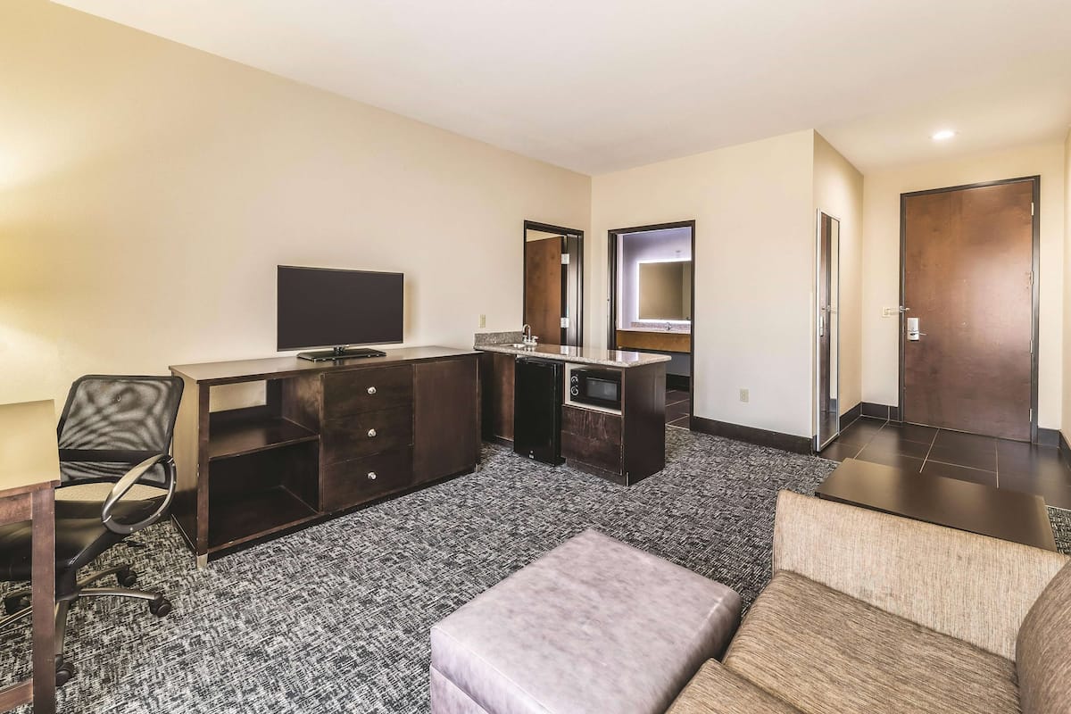 Ein Hotelzimmer mit Flachbildfernseher, Schreibtisch mit Schubladen, Spiegel, Sofa und Tür.