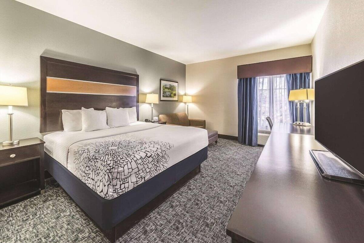 Ein Hotelzimmer mit einem großen Bett, zwei Nachttischen, einem Schreibtisch, einem Sessel und einem Fernseher.