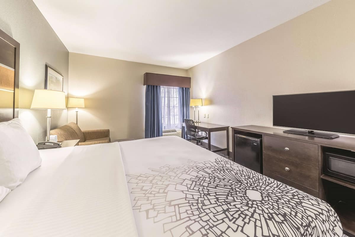 Ein Hotelzimmer mit einem großen Bett, einem Schreibtisch mit Stuhl, einem Fernseher und einer Minibar.