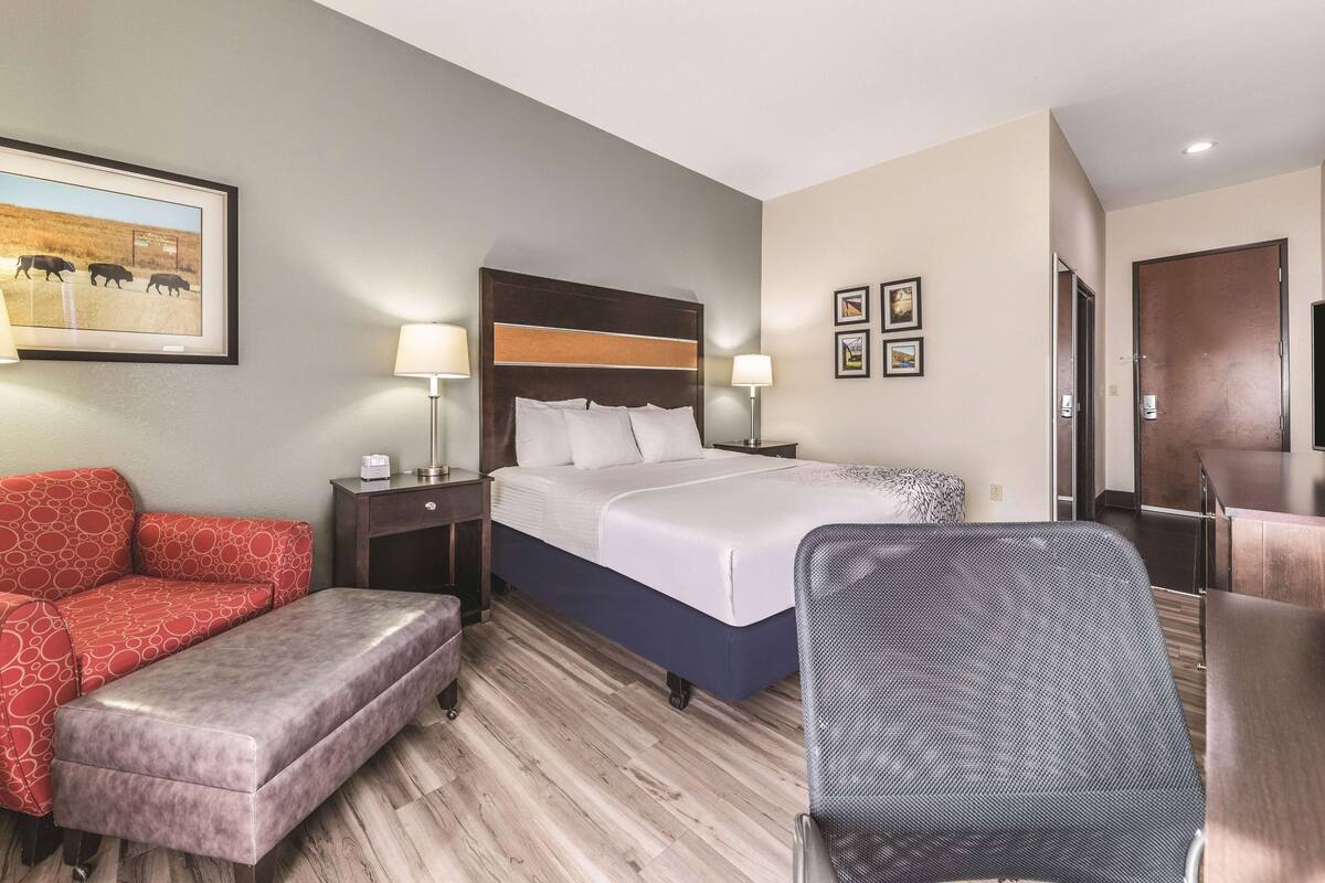 Ein Hotelzimmer mit Bett, Schreibtisch, Stuhl, Sofa und Nachttisch mit Lampe.