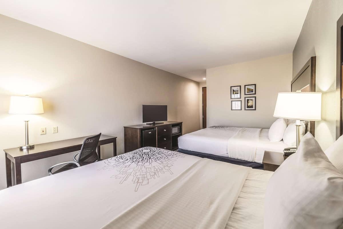 Ein Hotelzimmer mit zwei Betten, einem Schreibtisch, einem Stuhl, einem Fernseher und einer Lampe.