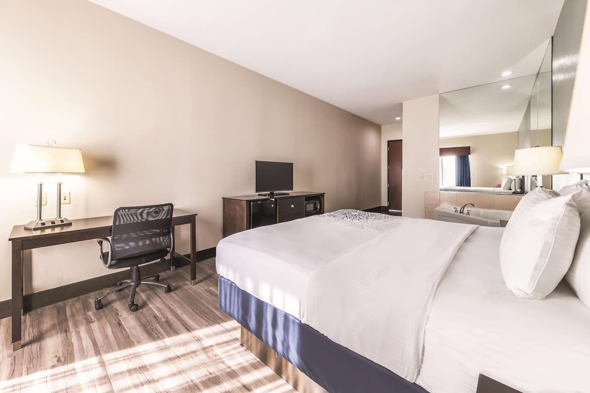 Ein Hotelzimmer mit Bett, Schreibtisch, Stuhl, Fernseher und einem großen Spiegel.