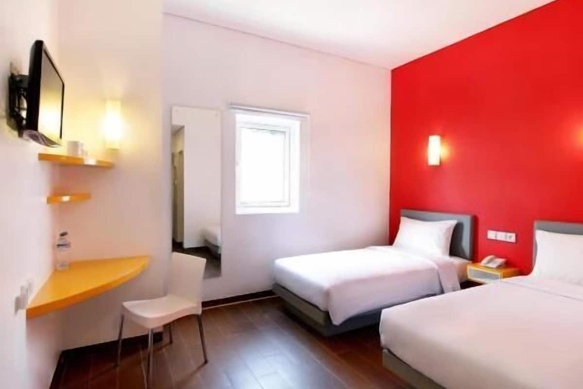Een hotelkamer met twee bedden, een bureau, een stoel, een televisie en een rode accentmuur.