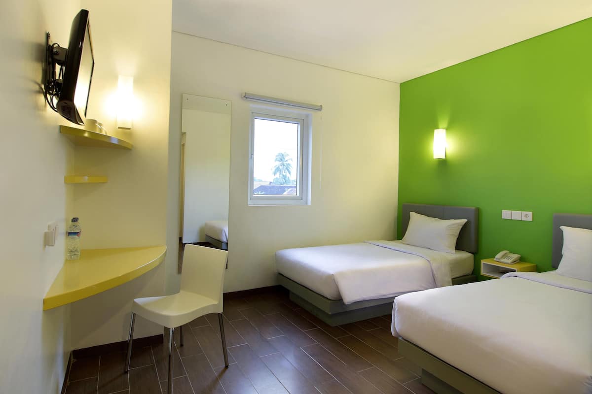 Een hotelkamer met twee bedden, een bureau met stoel, een televisie en een raam.