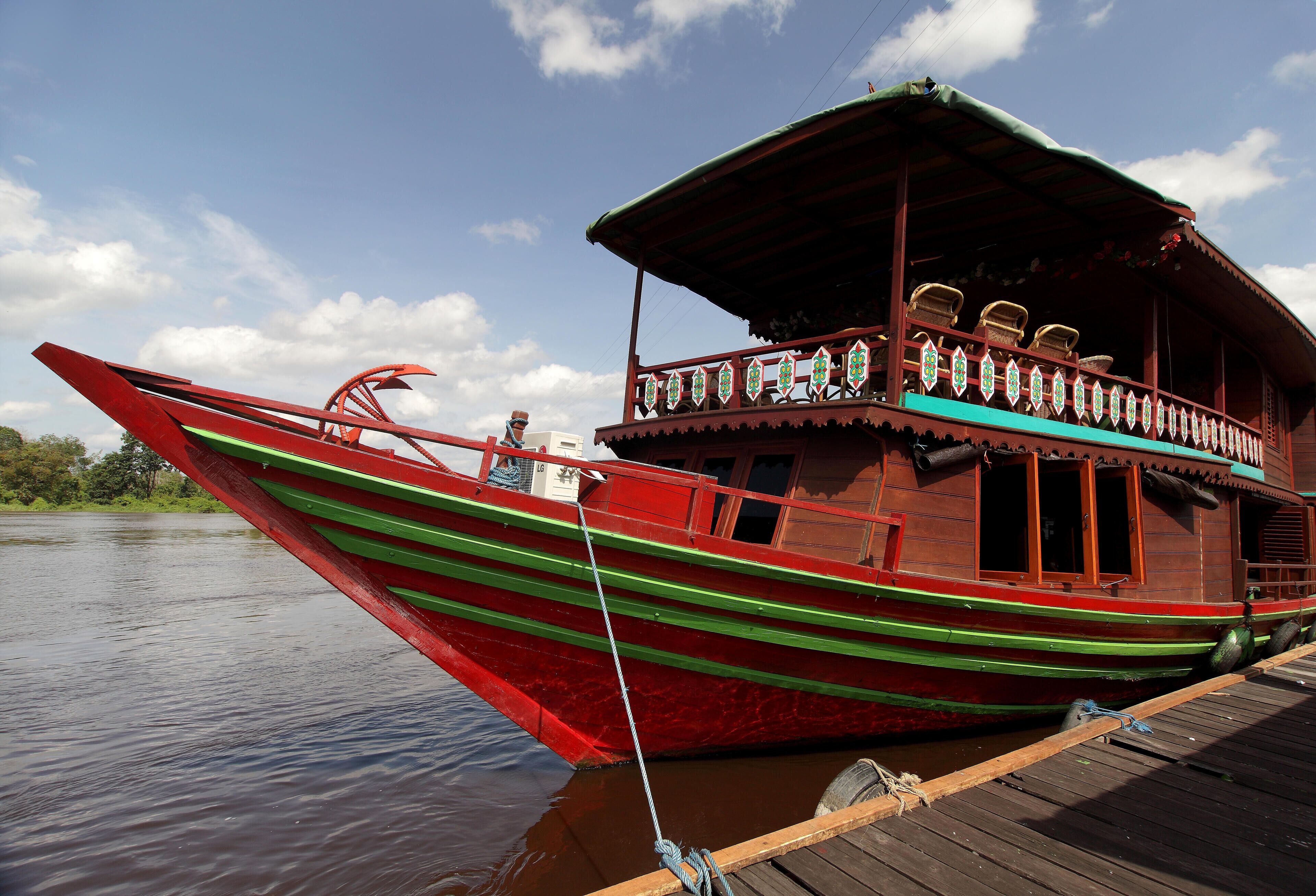 Un barco de madera tradicional con cubierta superior protegida, amarrado a un muelle de madera.