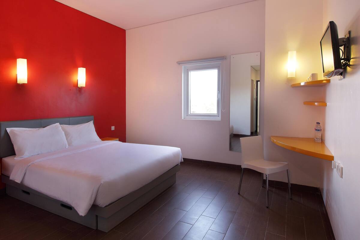 Een hotelkamer met een bed, een bureau, een stoel, een raam en een spiegel.