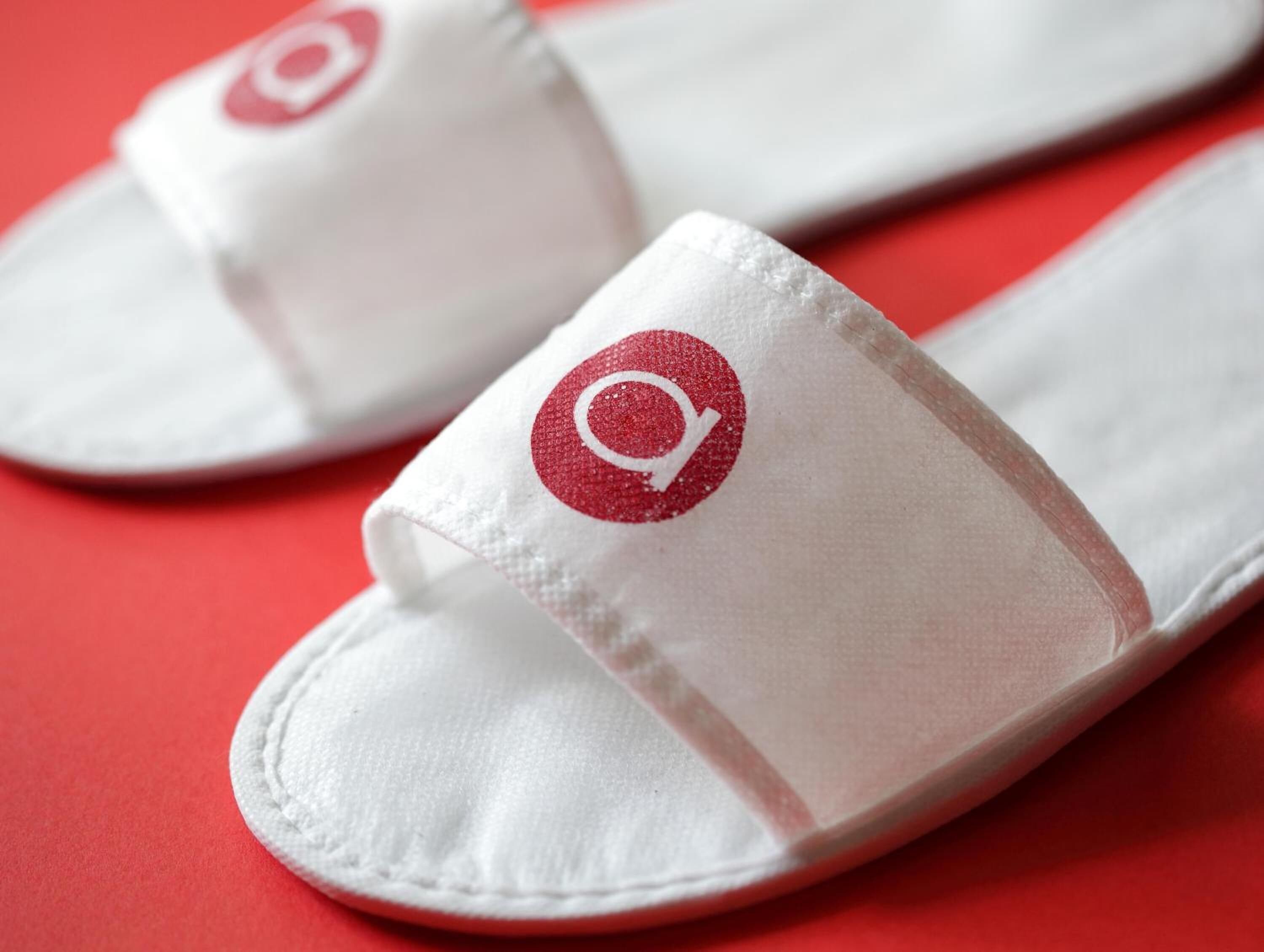 Une paire de pantoufles blanches ornées d’un logo rouge sur un fond rouge.